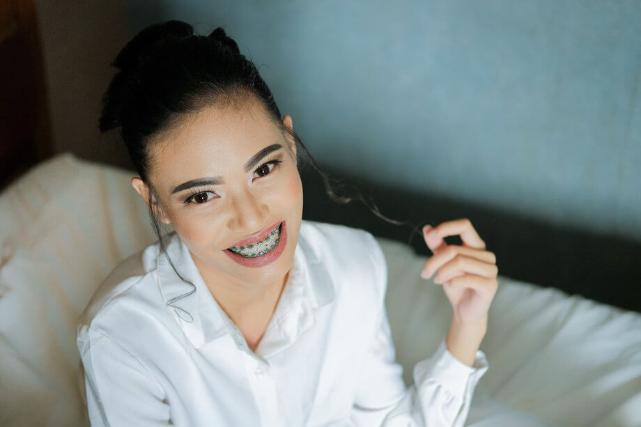 Young girl with brown hair and braces smiling while twirling her hair in a home setting.