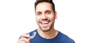 a man smiles while holding a clear aligner