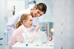 a mother and child smile while they brush their teeth